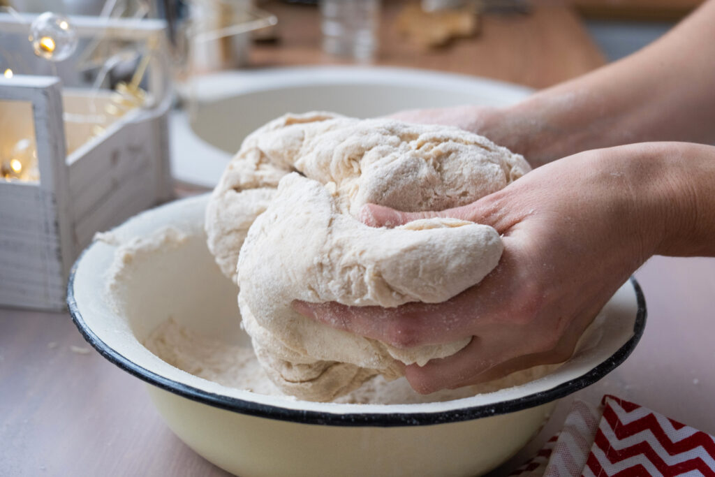 Hands knead thick dough on the kitchen table, decorated with festive decorations for Christmas and New year. Baking at home, aroma and comfort. Close-up