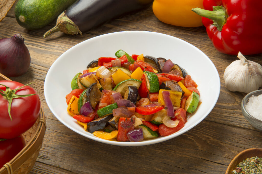 Ratatouille salad in a salad bowl on a wooden table with ingredients.