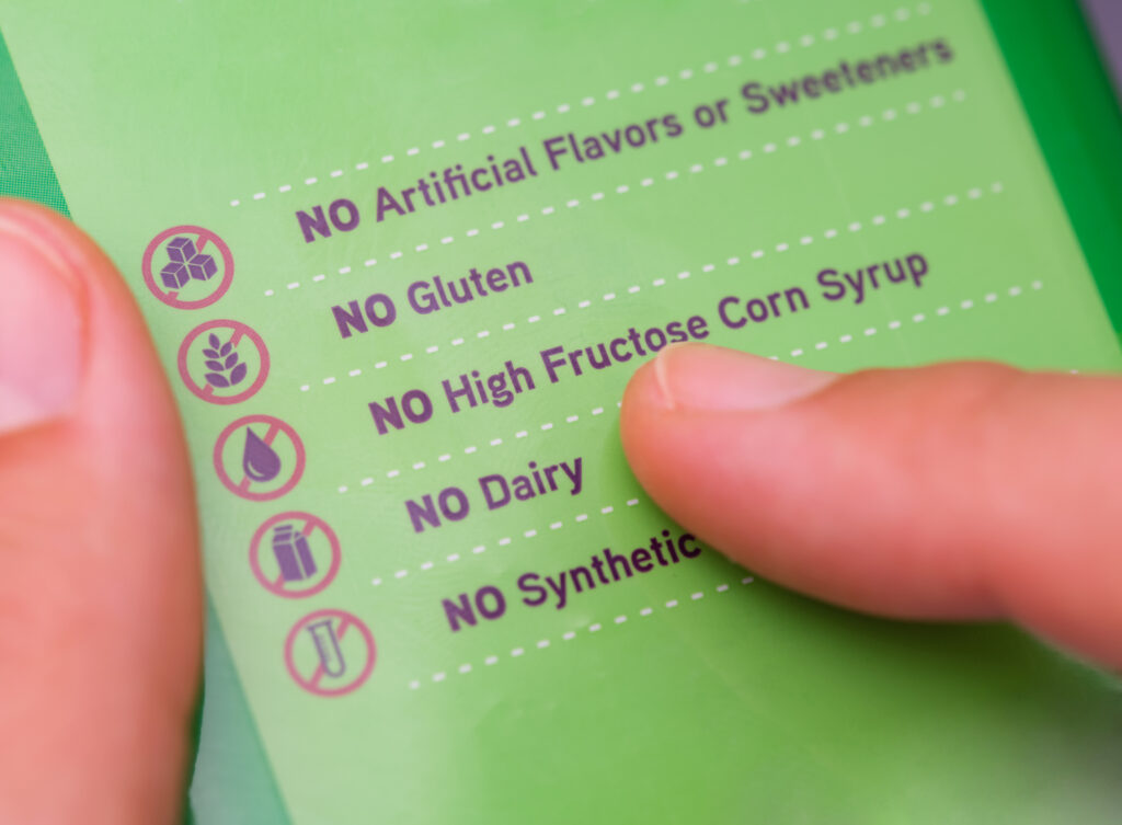 A person reading a label with the words No Artificial Flavors or Sweeteners, No gluten, No high fructose corn syrup, No dairy, No synthetics.